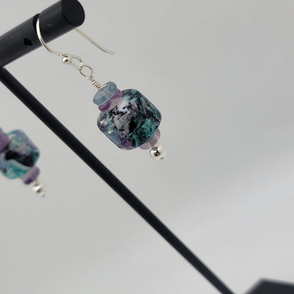 Multicolored beaded earrings on a stand against a gray background
