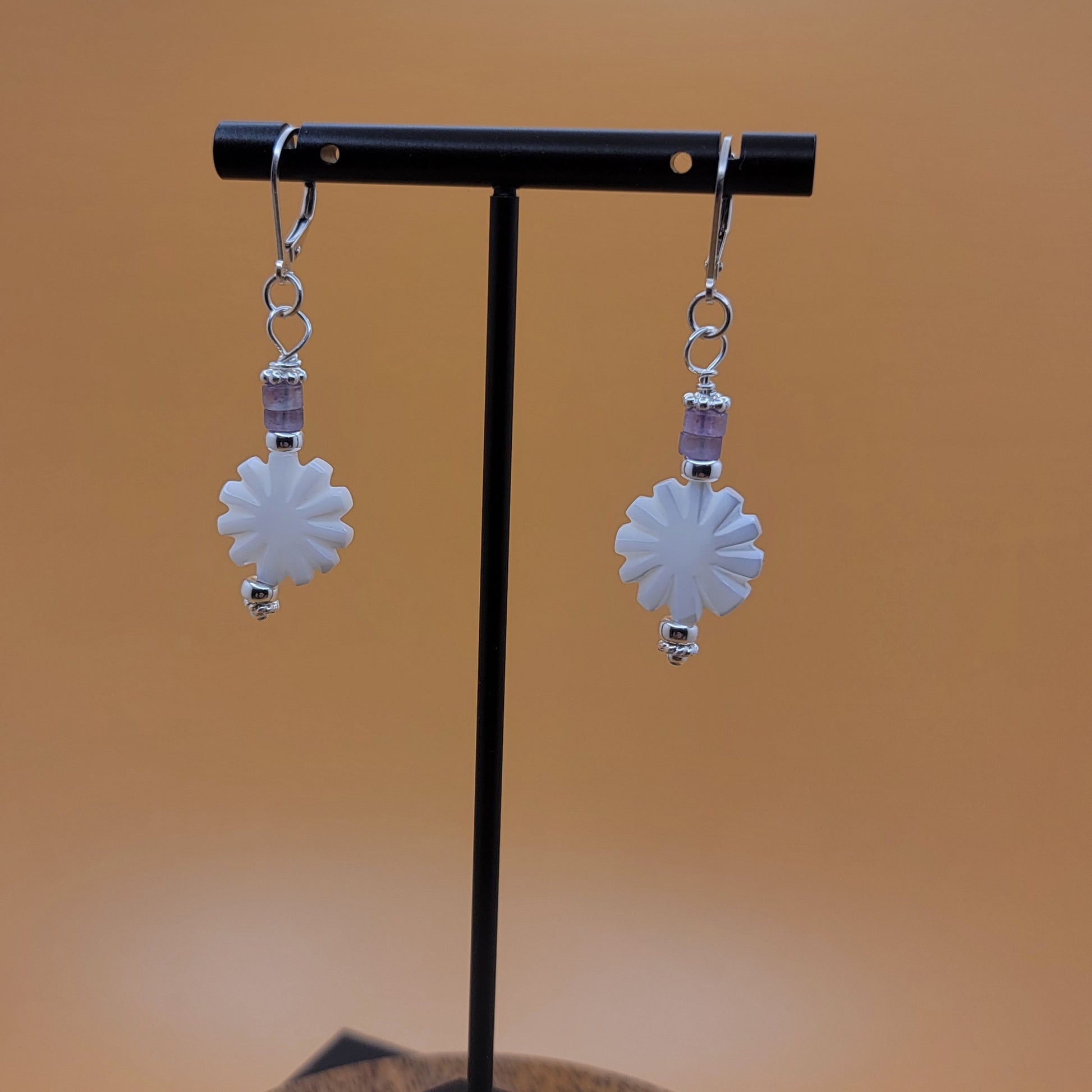 Flower-shaped earrings on a black stand with a blurred brown background