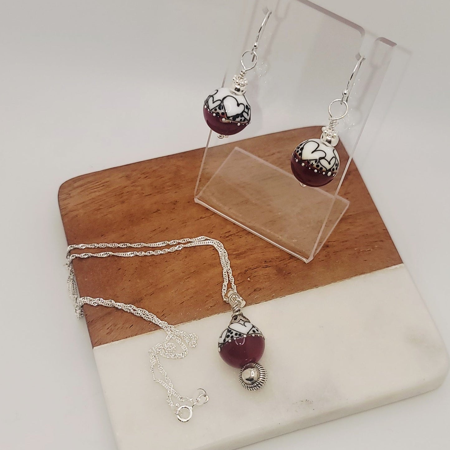 Jewelry set with maroon beads and silver accents on a wooden and stone surface.