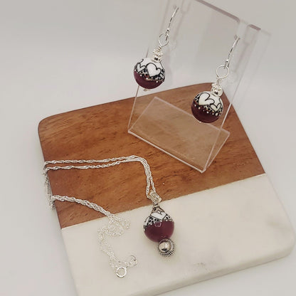 Jewelry set with maroon beads and silver accents on a wooden and stone surface.