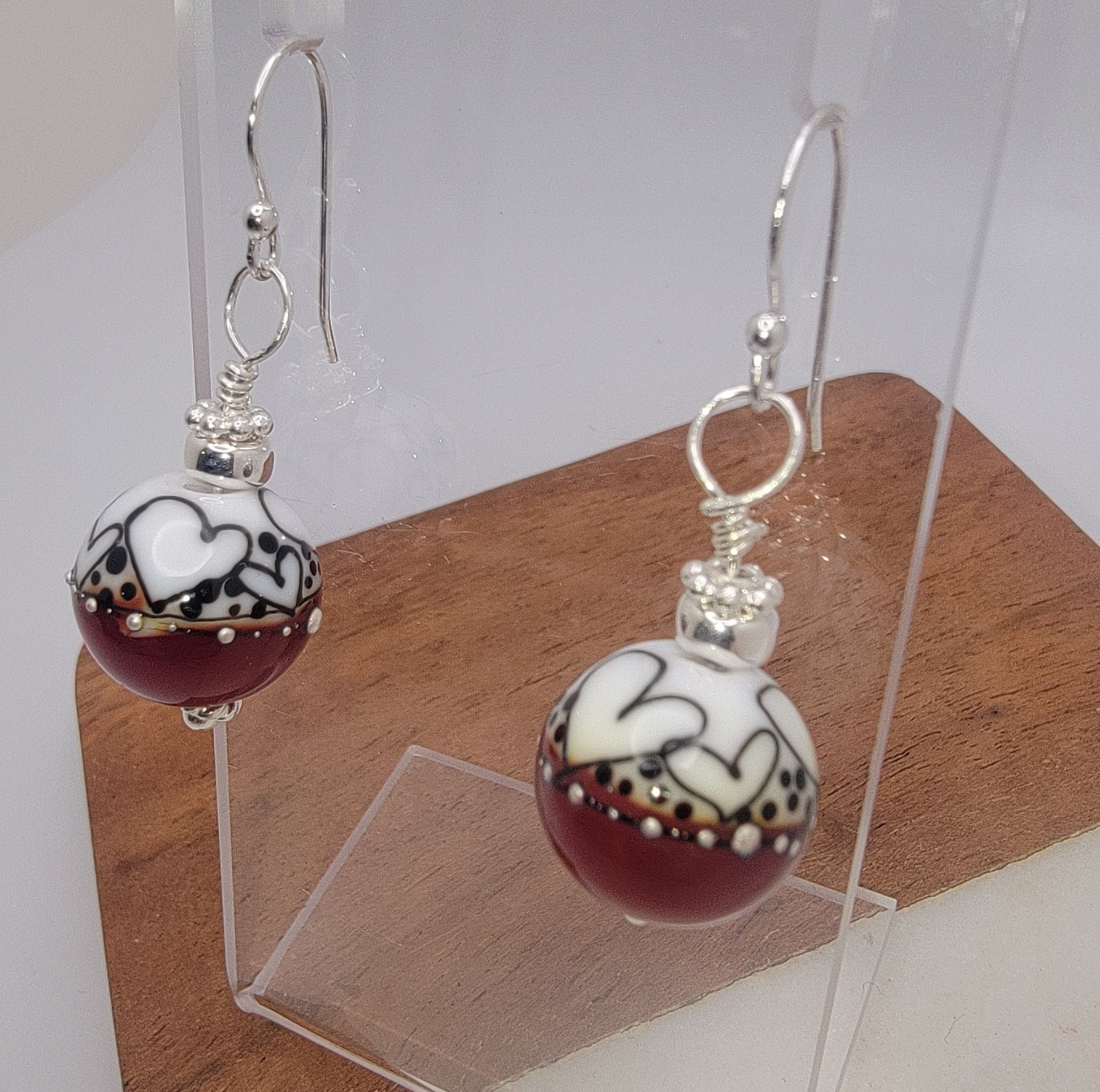 Pair of earrings with maroon and white heart designs on a wooden block.