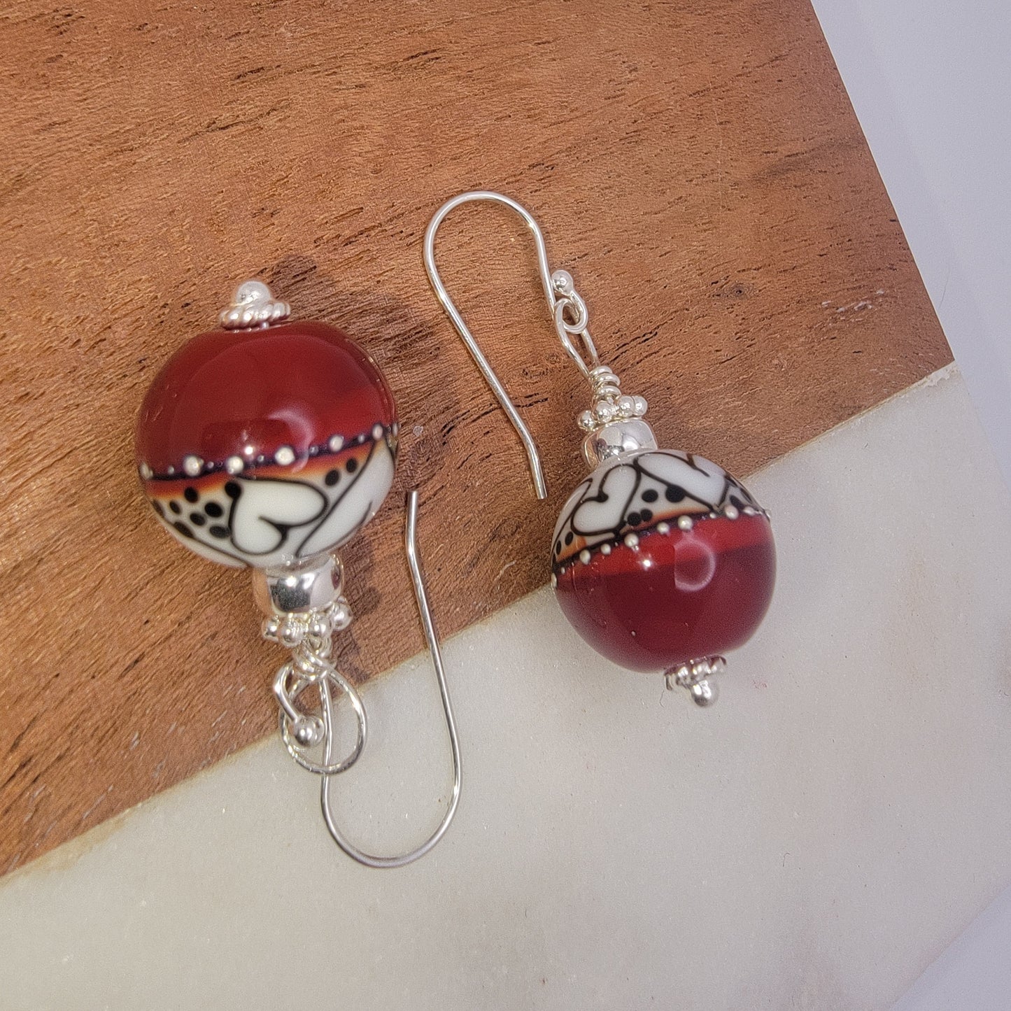 Pair of earrings with red and white spherical beads on a wooden surface