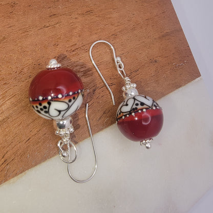 Pair of earrings with red and white spherical beads on a wooden surface