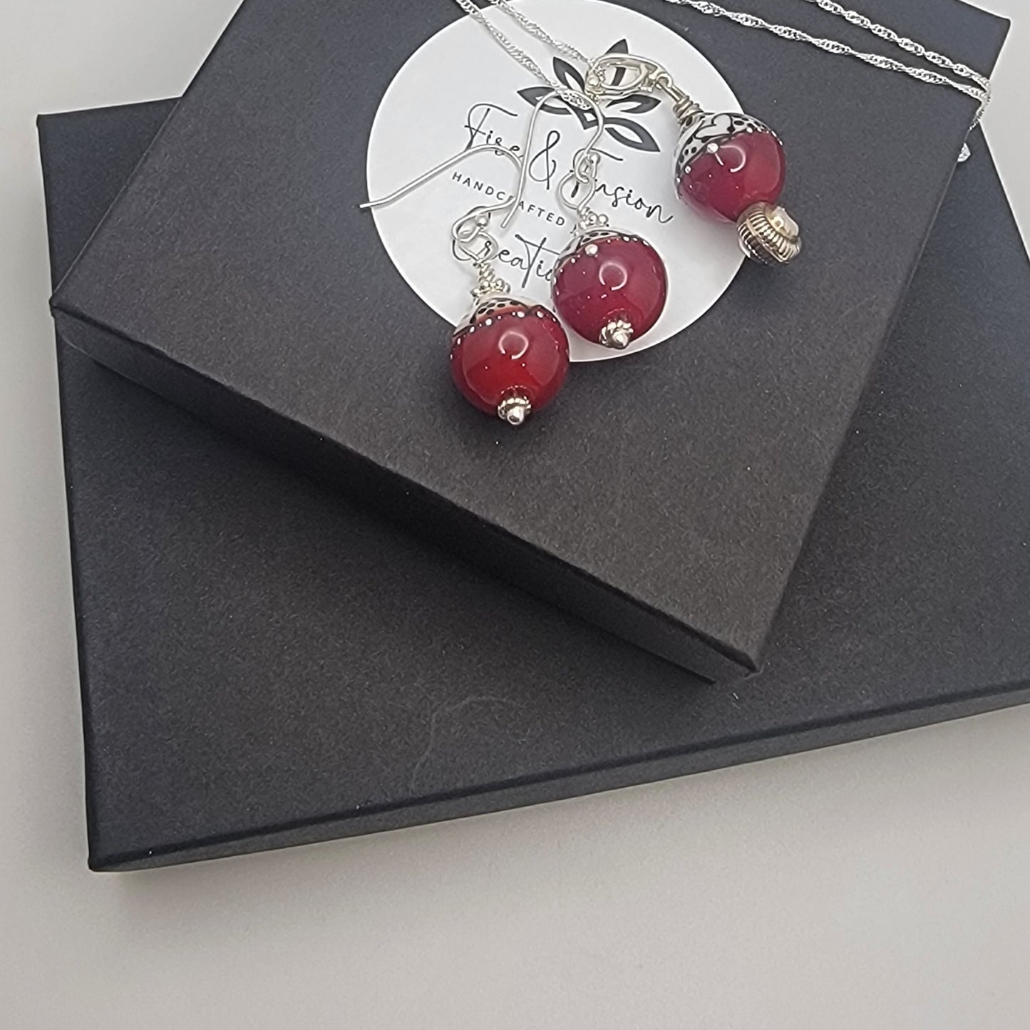 Necklace with red beads on a branded card inside a black box