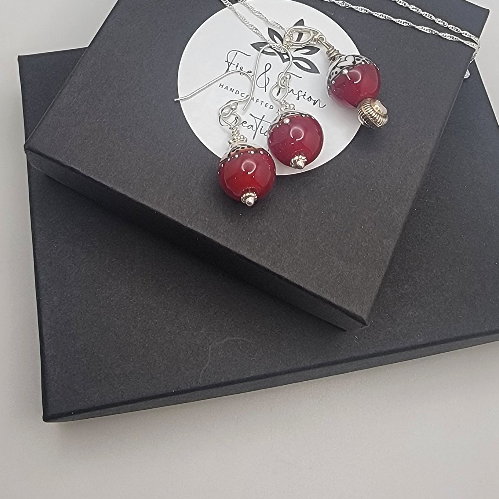 Necklace with red beads on a branded card inside a black box