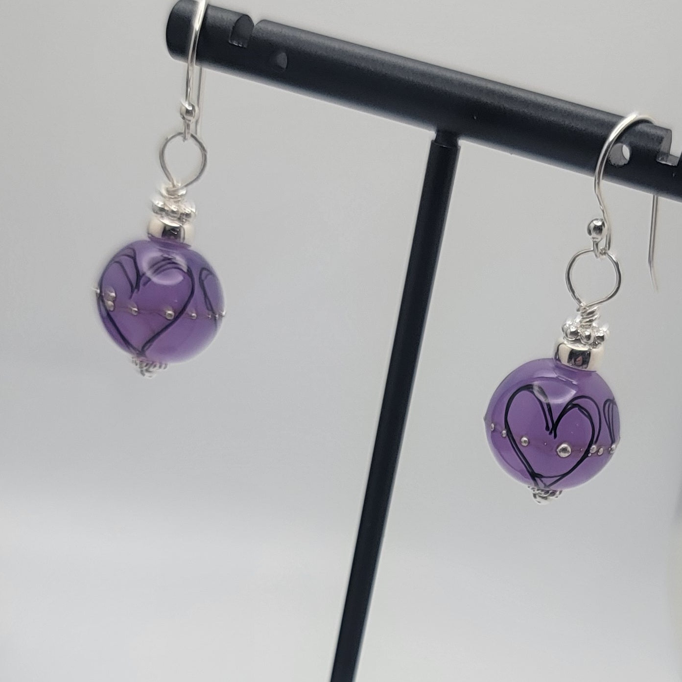 Purple heart-shaped earrings on a black stand against a light gray background
