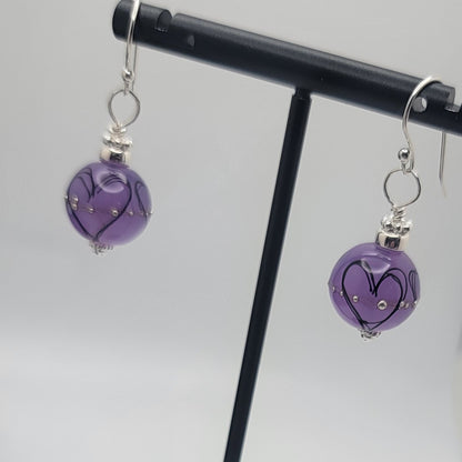 Purple heart-shaped earrings on a black stand against a light gray background