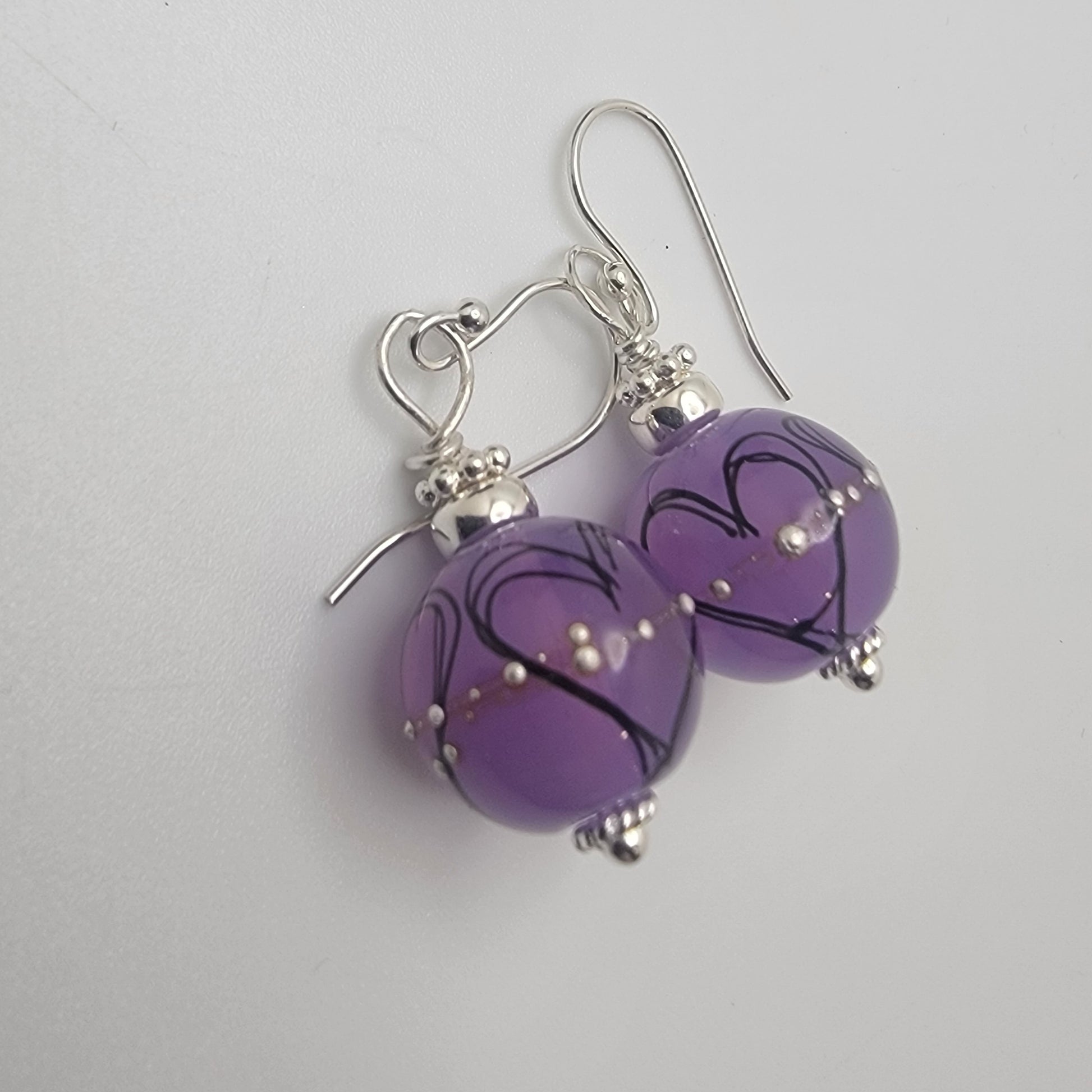 Purple heart-shaped earrings with silver accents on a light gray background