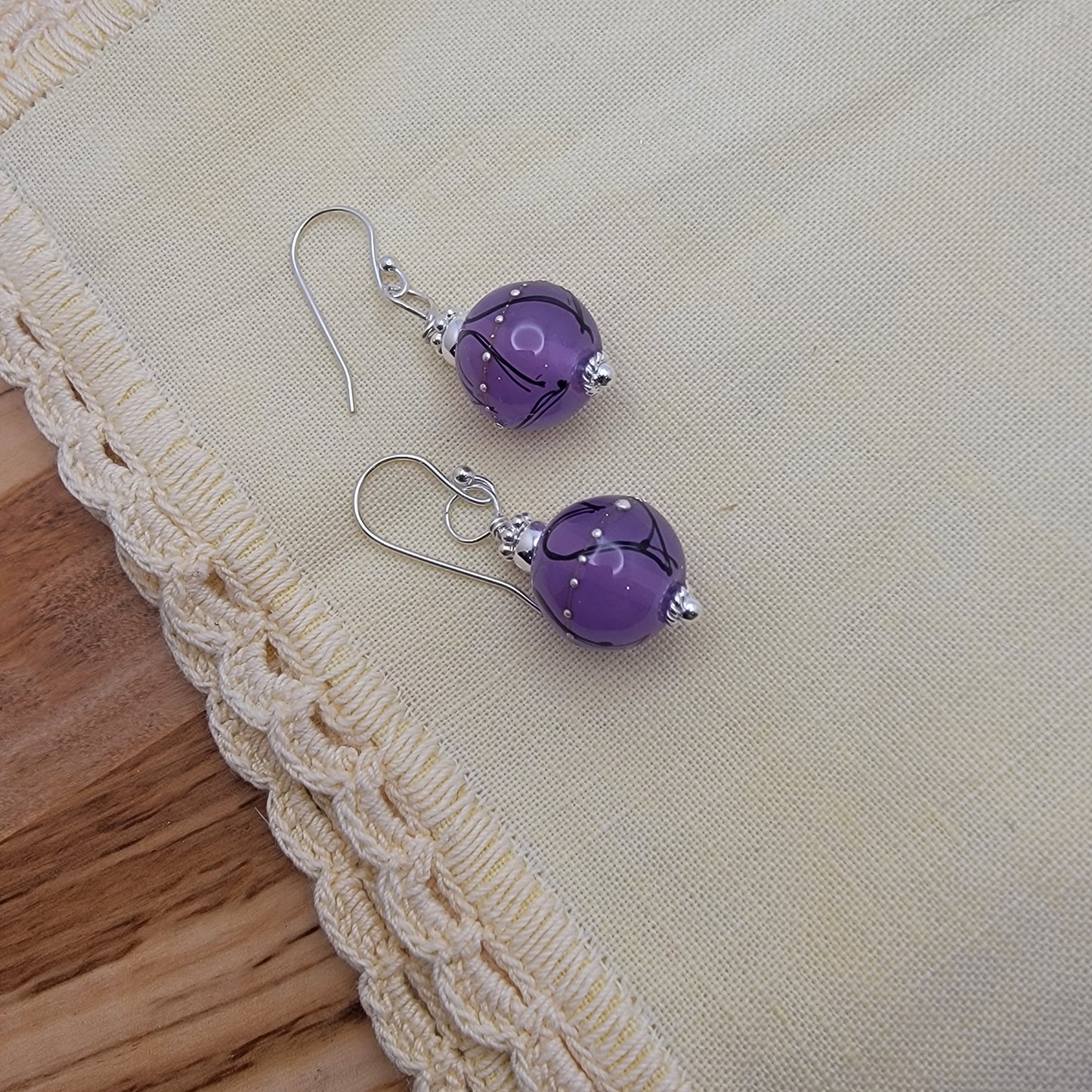 Purple glass earrings on a beige fabric background