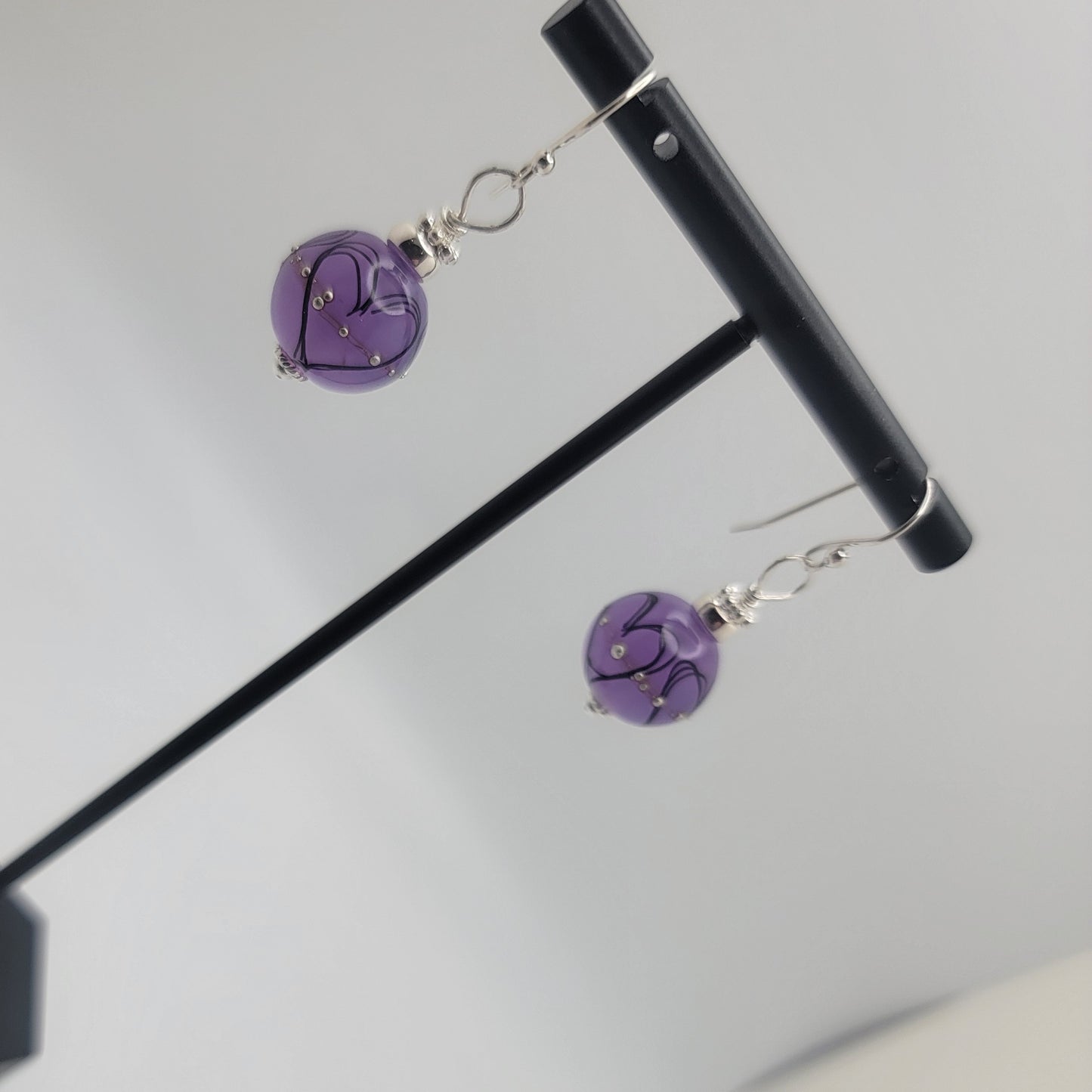 Purple heart-shaped earrings on a stand against a light gray background