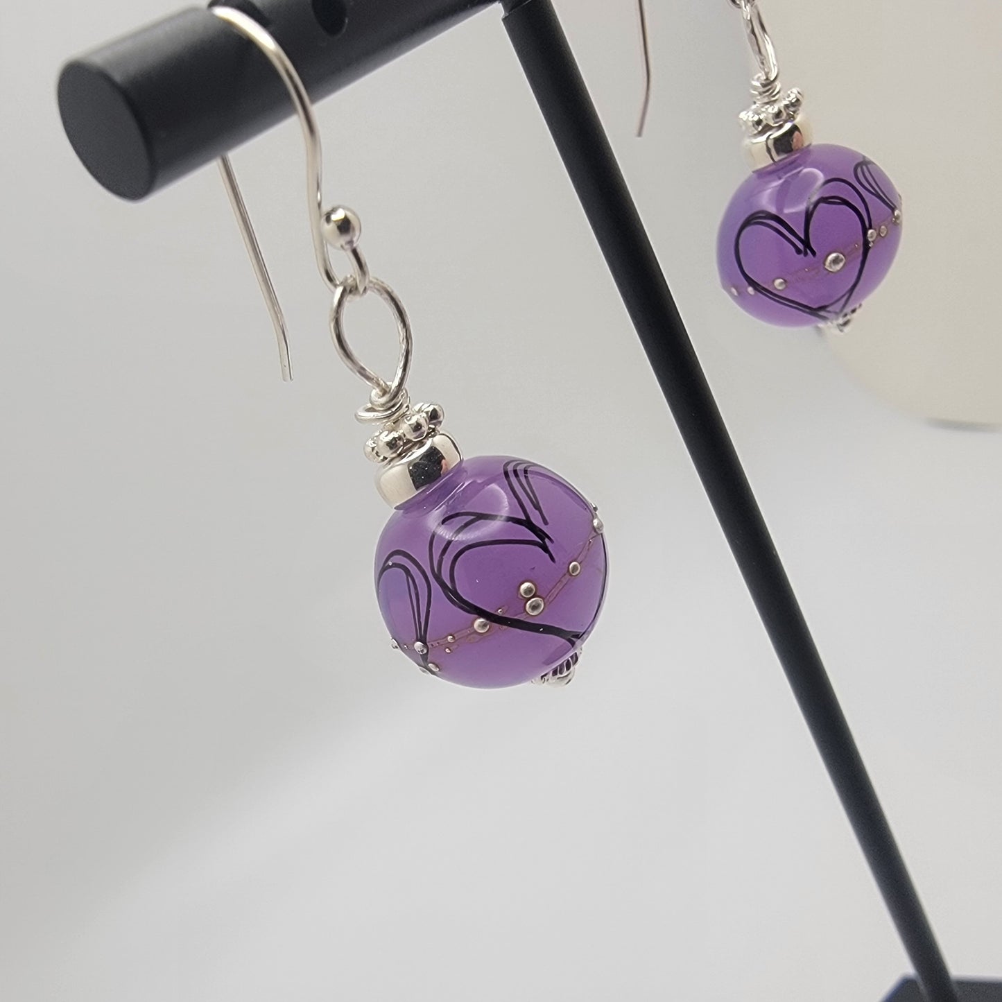 Purple earrings with silver hooks on a stand against a gray background