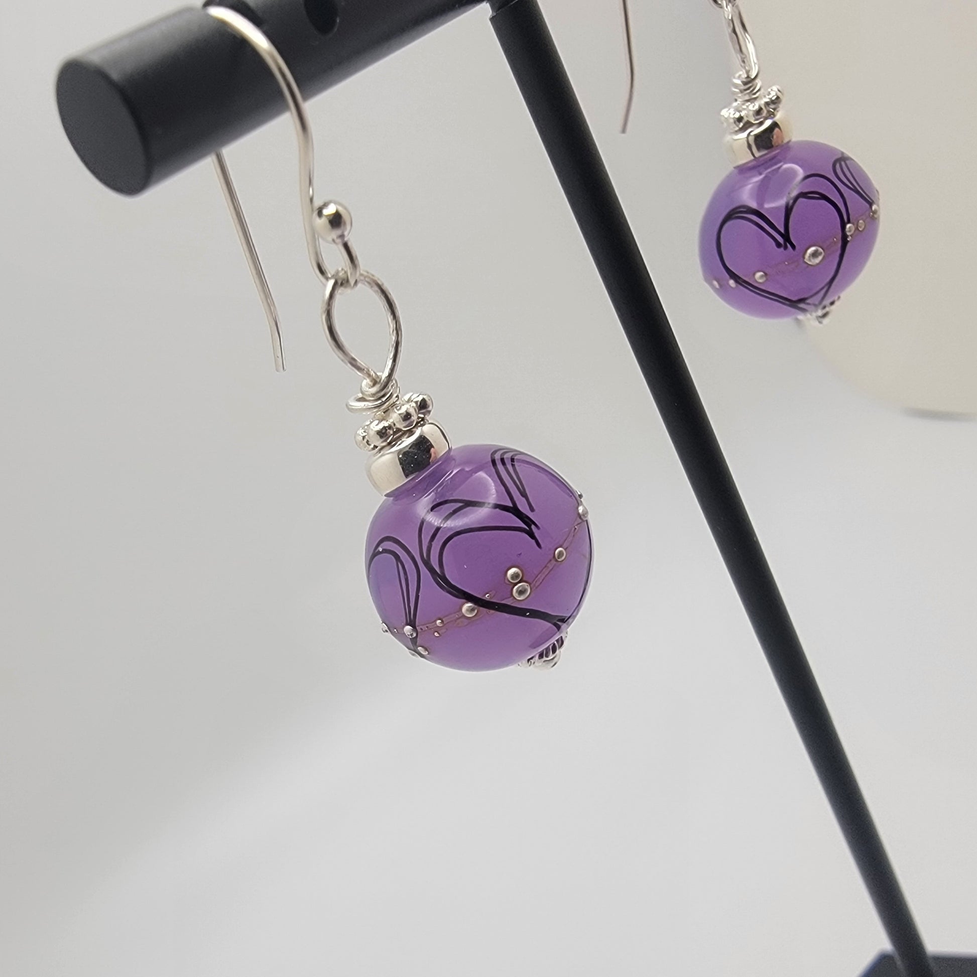 Purple earrings with silver hooks on a stand against a gray background