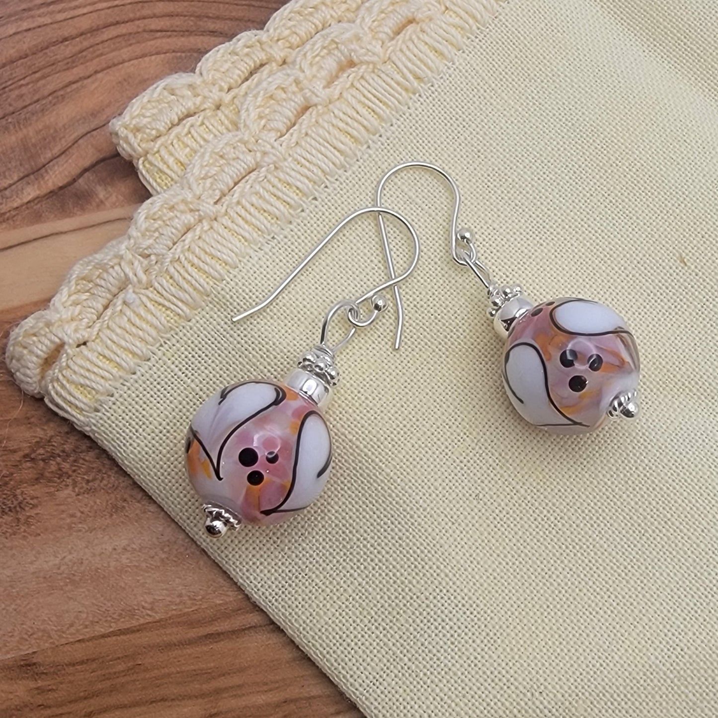 Pair of earrings with marbled pink and white beads on a beige fabric background