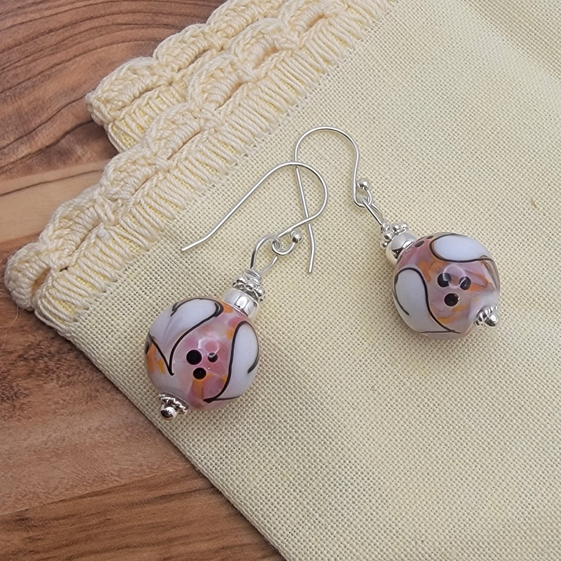 Pair of earrings with marbled pink and white beads on a beige fabric background