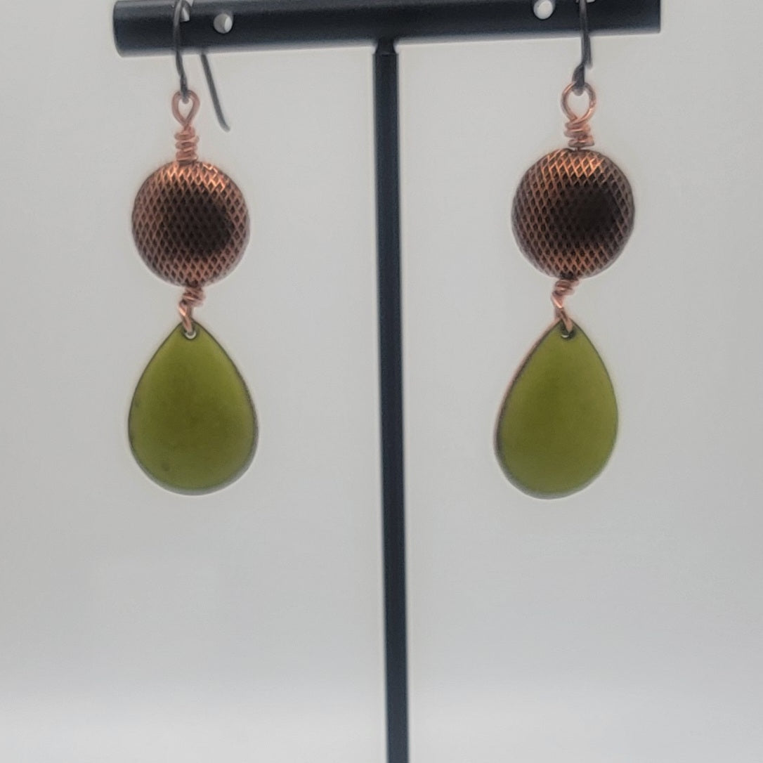 Pair of earrings with green teardrop-shaped beads and copper accents on a stand.
