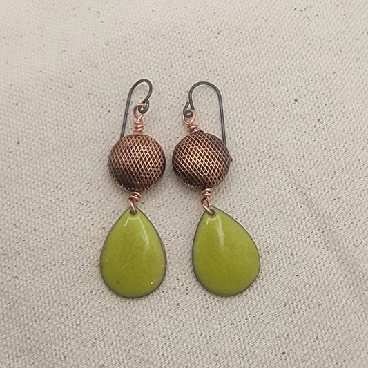 Pair of earrings with green teardrop-shaped stones and copper mesh balls on a beige fabric background.