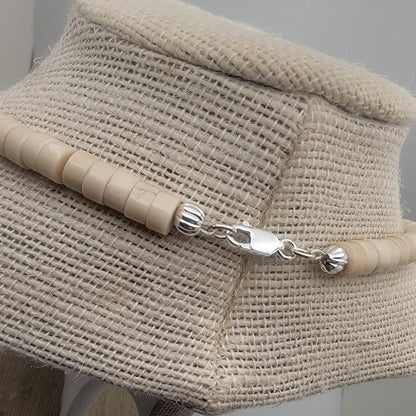 Necklace close up of silver clasp with beige beads on a textured surface