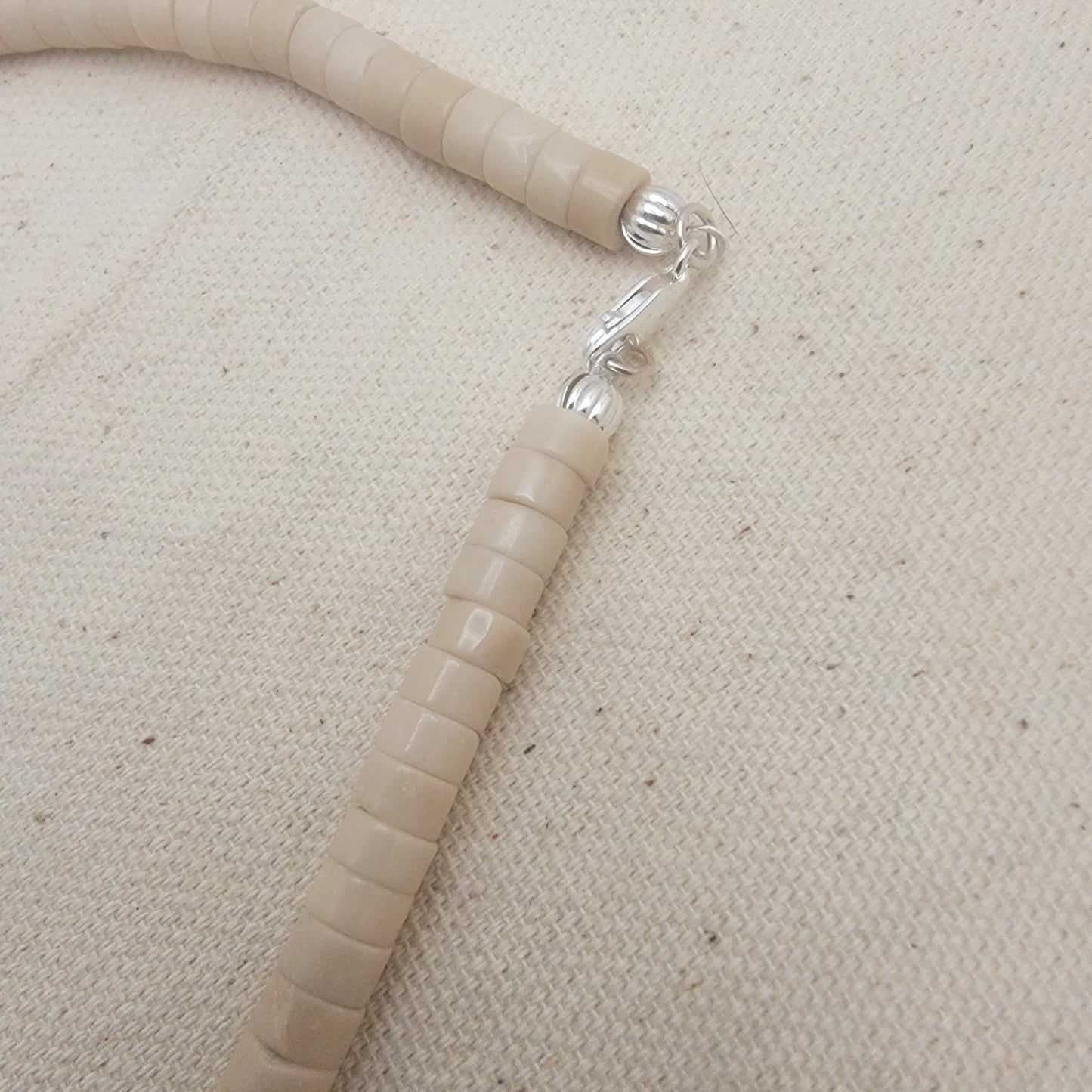 Silver clasp with beige beads on a beige fabric background