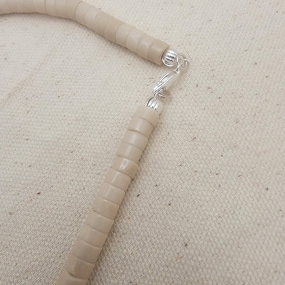 Silver clasp with beige beads on a beige fabric background