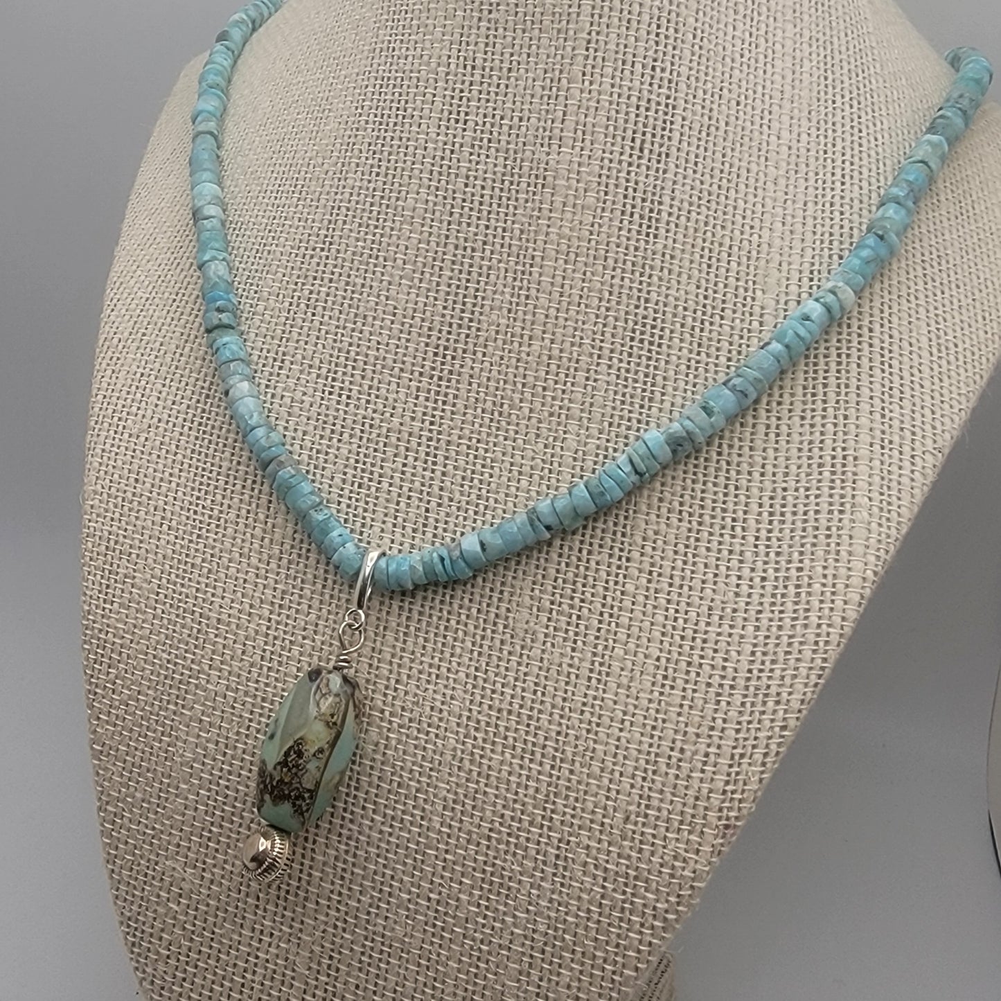 Larimar beaded necklace with an agate pendant on a beige fabric surface