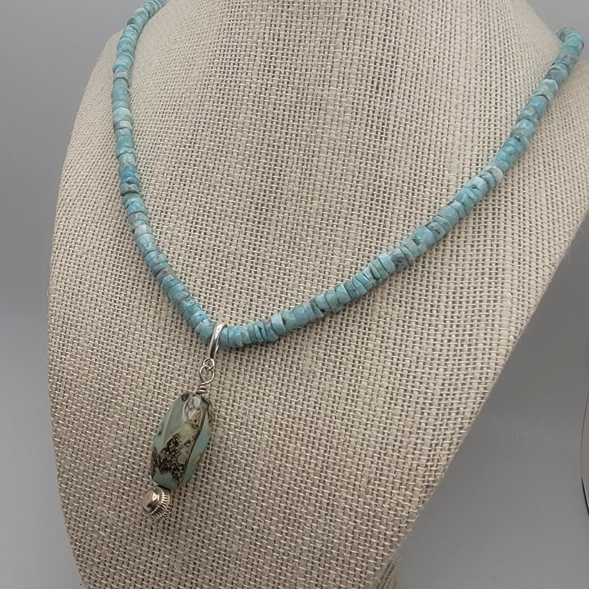 Larimar beaded necklace with an agate pendant on a beige fabric surface