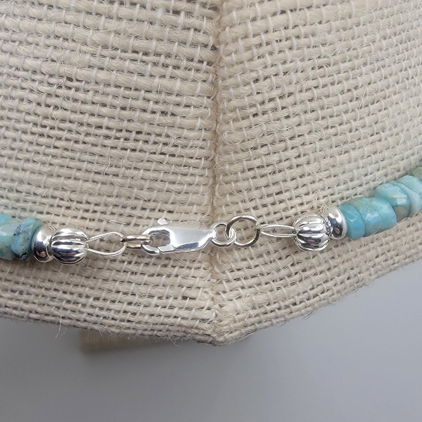 Silver necklace clasp with larimar beads on a textured beige background