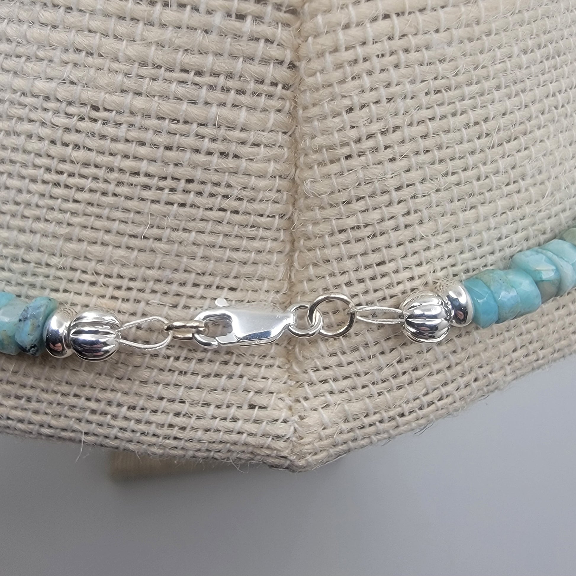 Silver necklace clasp with larimar beads on a textured beige background