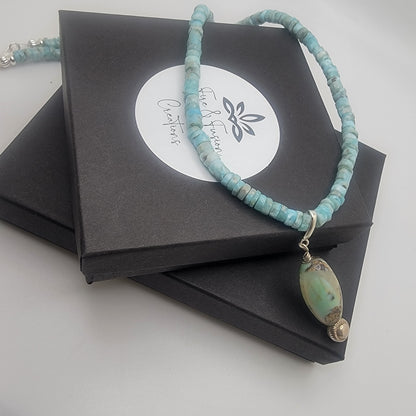 Larimar beaded necklace with a large pendant on a black box with a brand label.