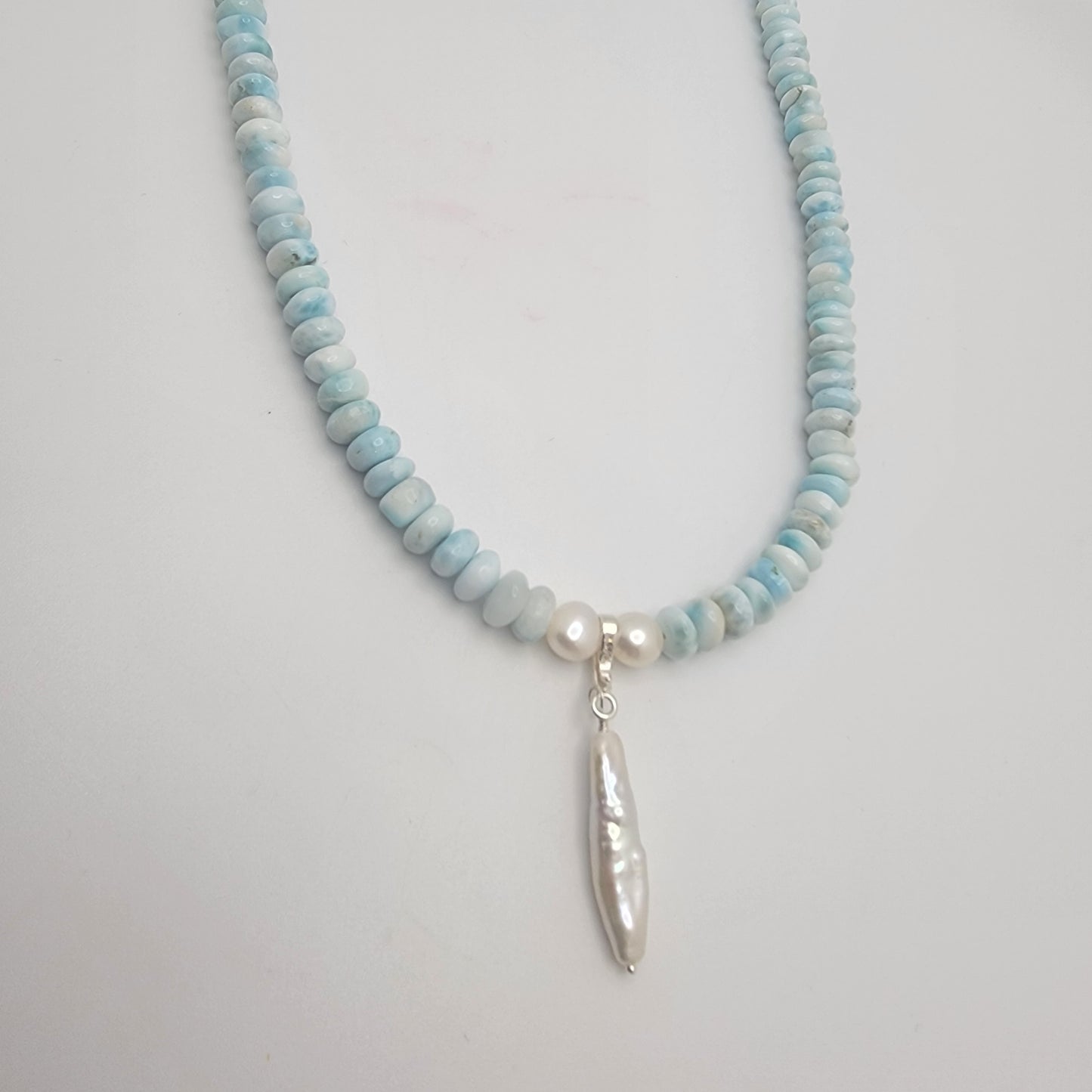 Necklace with blue and white beaded chain and pearl pendant on a light gray background