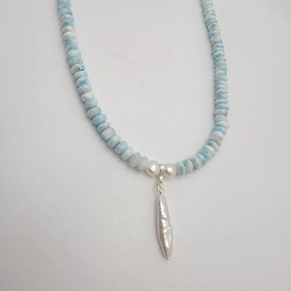 Necklace with blue and white beaded chain and pearl pendant on a light gray background