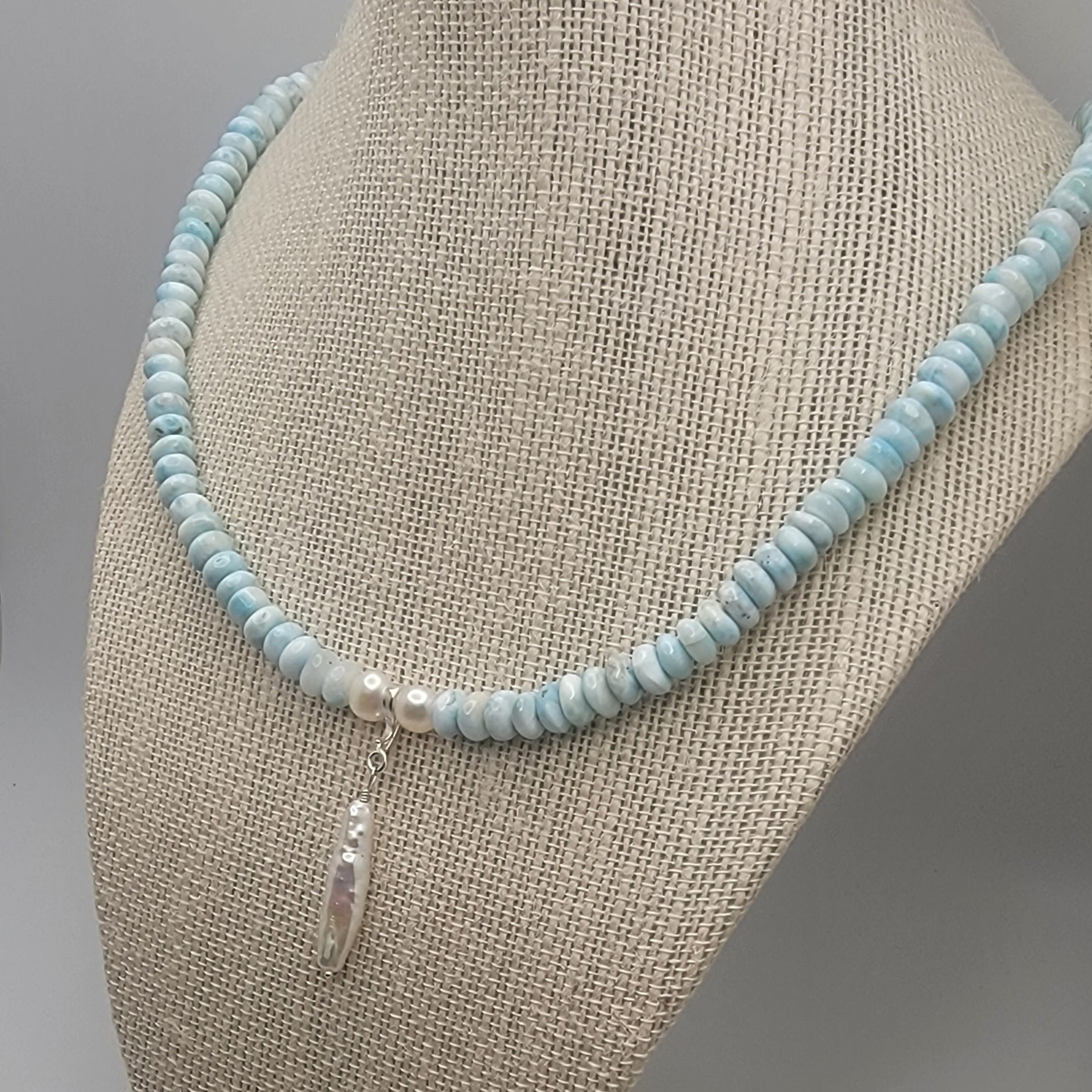 Beaded necklace with a pearl pendant on a mannequin bust against a neutral background