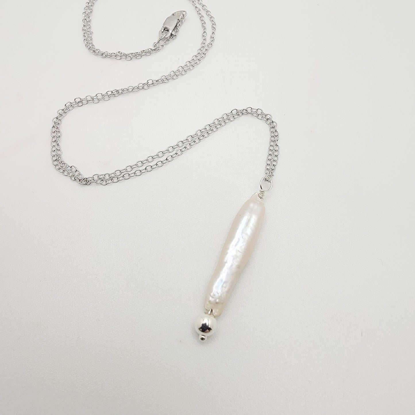 Silver necklace with a stick pearl pendant on a light gray background