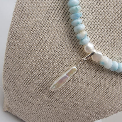 Beaded necklace with a pearl and silver bail on a textured beige surface