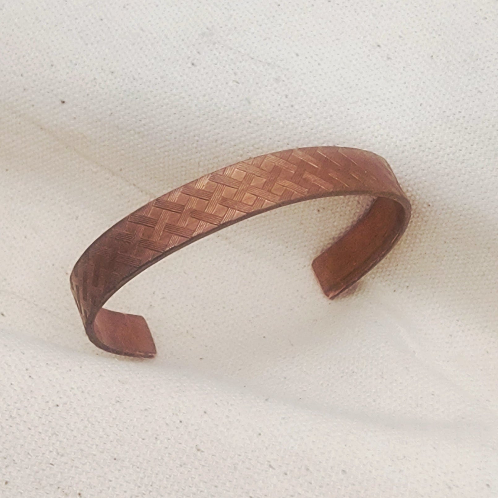 Copper woven bracelet on a textured beige surface
