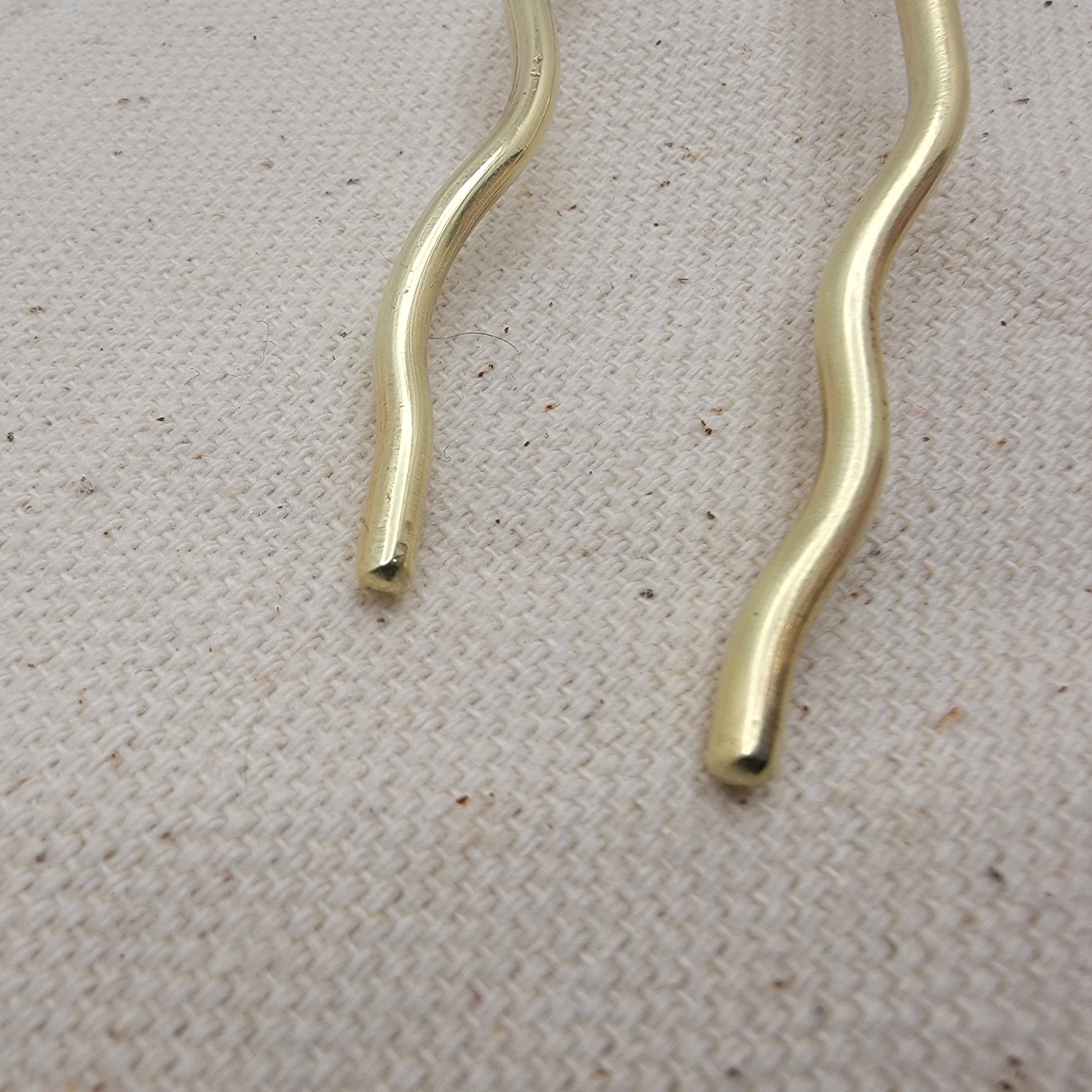 Close up of ends of brass hair pin on a textured beige surface