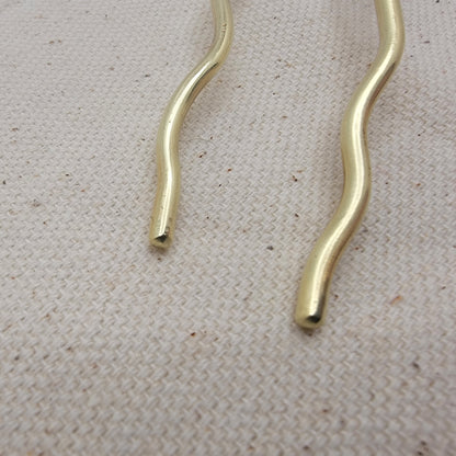 Close up of ends of brass hair pin on a textured beige surface