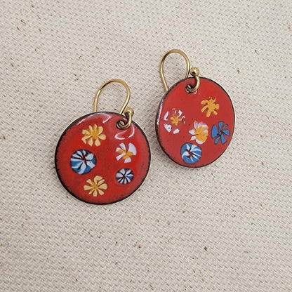 Pair of red earrings with floral patterns on a beige fabric background