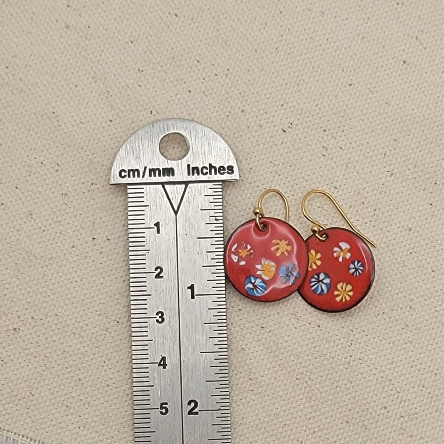 Red floral earrings next to a ruler on a beige background