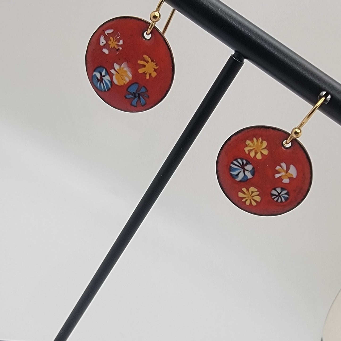 Red circular earrings with floral designs hanging on a stand against a white background