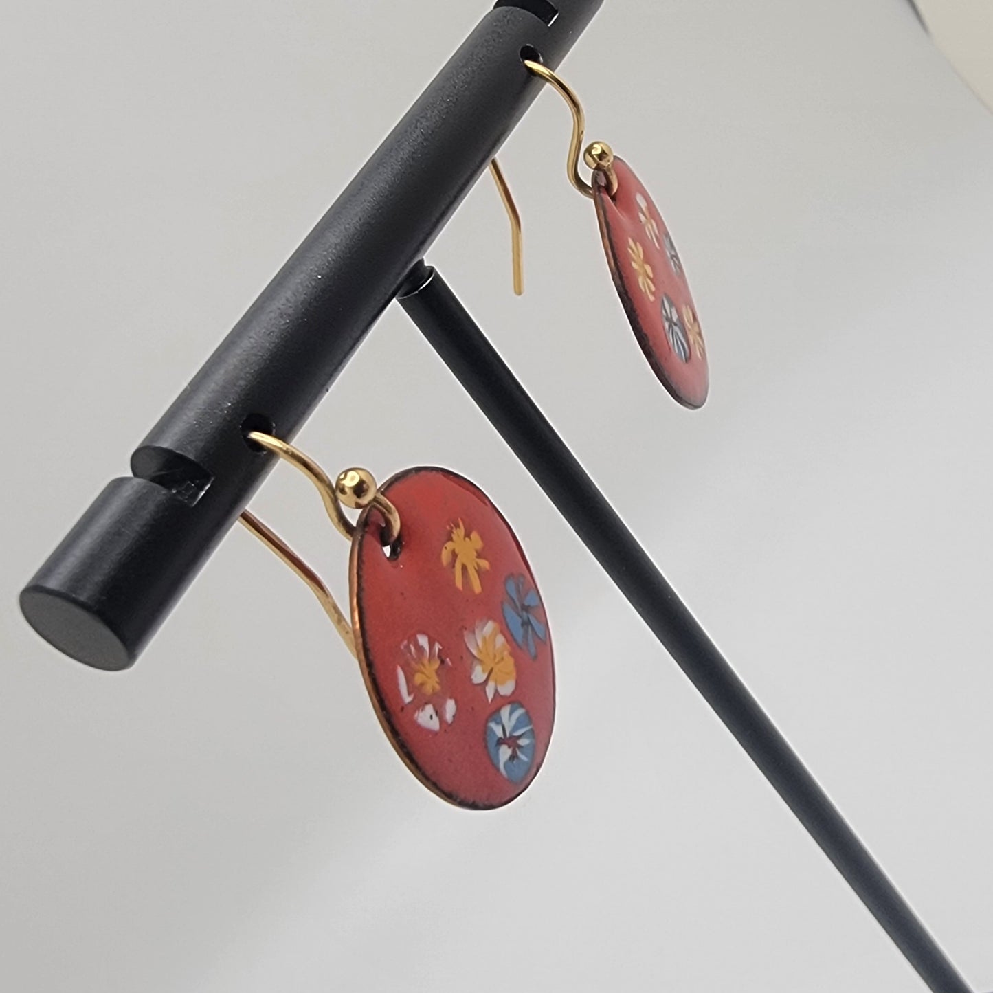 Pair of earrings with floral designs on a black stand against a light gray background