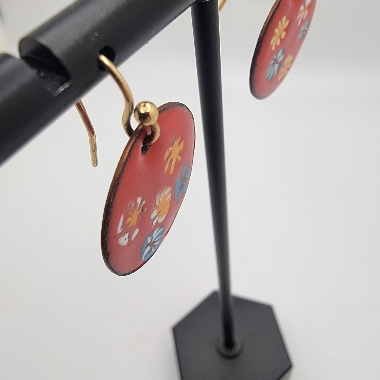 Red floral earrings on a black stand against a white background