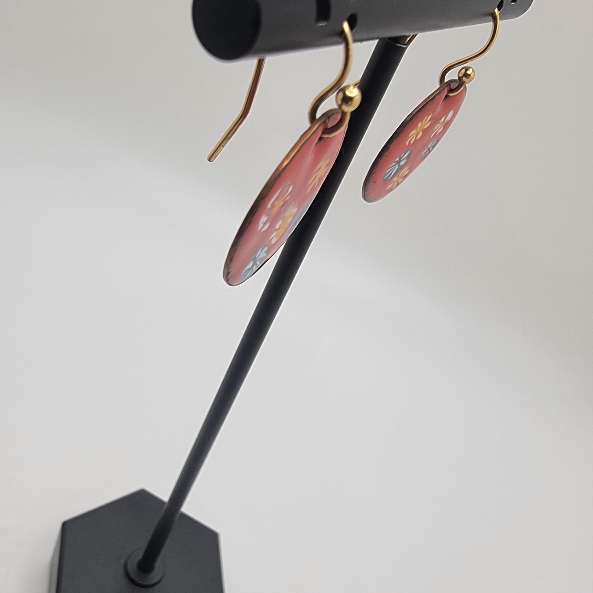 Red earrings on a black stand against a white background