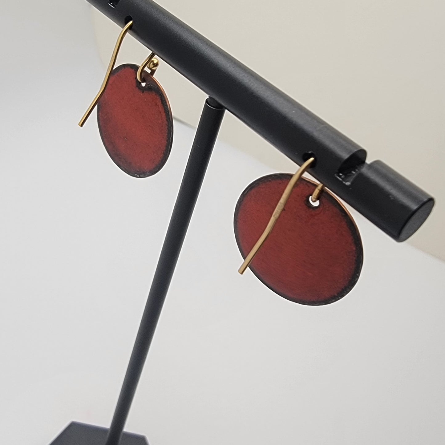 Red circular earrings on a black stand against a white background