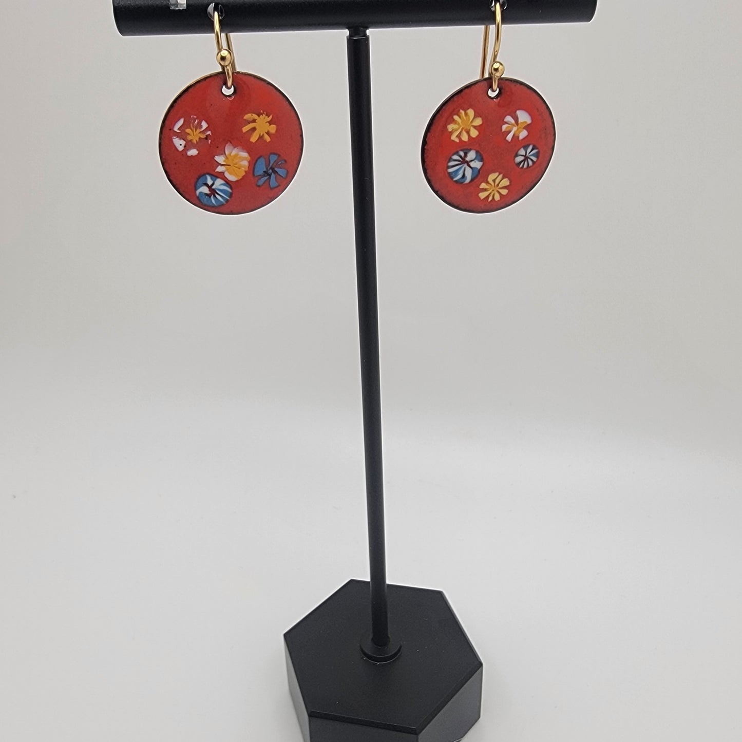 Red circular earrings with floral designs on a black stand against a white background