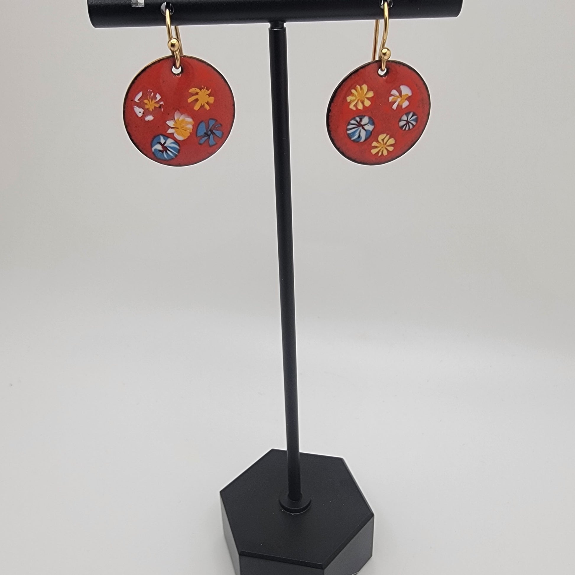 Red circular earrings with floral designs on a black stand against a white background
