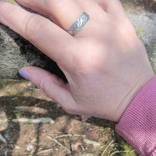 Hand wearing a silver ring with a natural background