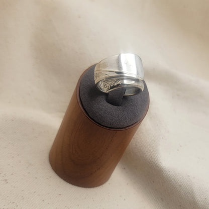 Silver ring on a gray and wood ring stand on a beige fabric background