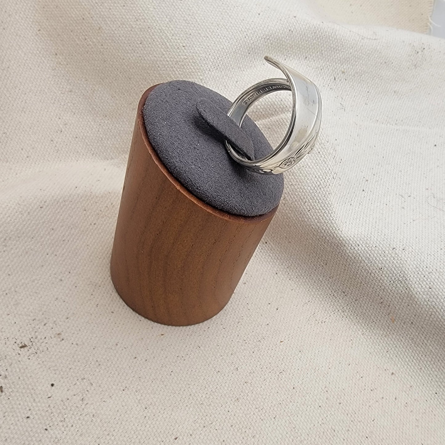 Silver ring on a gray and wood ring stand on a beige fabric background