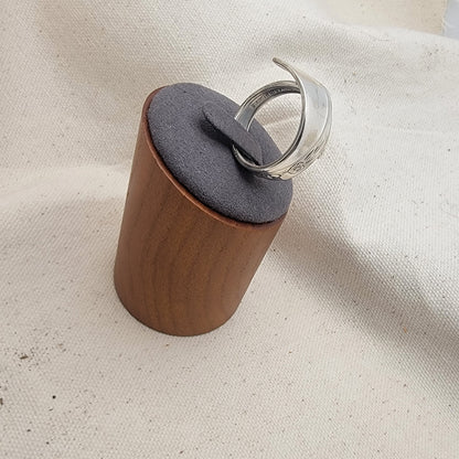 Silver ring on a gray and wood ring stand on a beige fabric background
