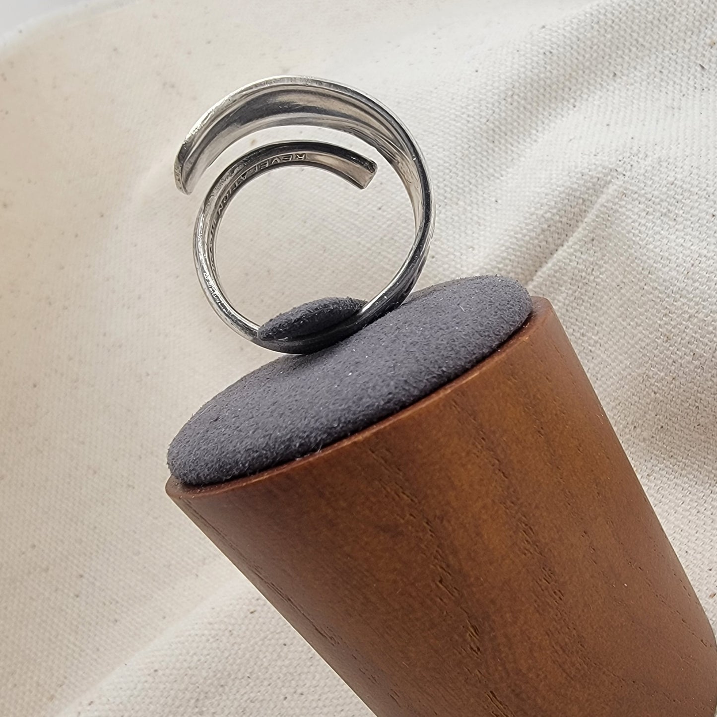 Silver ring on a gray and wood ring stand on a beige fabric background